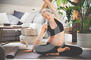 Young beautiful pregnant woman training yoga at home in her living room. Motherhood, pregnancy, healthy lifestyle and