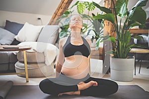 Young beautiful pregnant woman training yoga at home in her living room. Motherhood, pregnancy, healthy lifestyle and