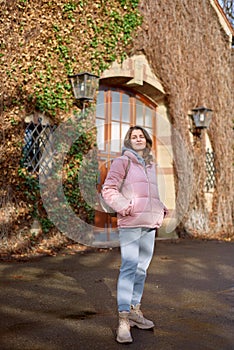 Young beautiful pretty tourist girl in warm hat and coat with backpack walking at cold autumn in Europe city enjoying
