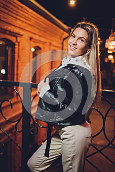 Young beautiful pretty woman smiling and posing at city street in the night against evening lights bokeh background.