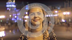 Young beautiful pretty woman smiling and posing at city street in the night against evening lights bokeh background