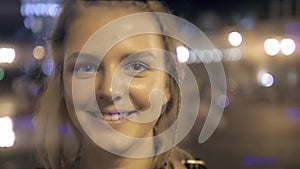 Young beautiful pretty woman smiling and posing at city street in the night against evening lights bokeh background