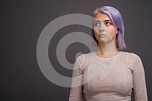 Young beautiful rebel woman with colorful hair against gray back