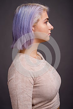 Young beautiful rebel woman with colorful hair against gray back