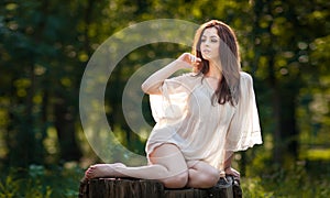 Giovane bellissimo capelli una donna logorante trasparente bianco camicetta posa sul tronco d'albero verde foresta alla moda 