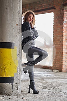 Young beautiful red-haired fashionable girl in a black jacket and black leather leather pants, in boots on a high platform