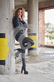 Young beautiful red-haired fashionable girl in a black jacket and black leather leather pants, in boots on a high platform