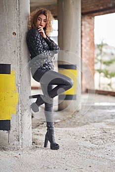 Young beautiful red-haired fashionable girl in a black jacket and black leather leather pants, in boots on a high platform