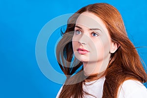 Young beautiful red-haired girl with hair developing in the wind dreamily looks upwards. Studio shot, skin retouch