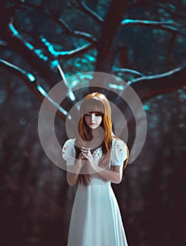 Young beautiful red-haired lady girl, stands in mystical dark deep dense forest hands folded in prayer. Night background