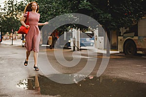 Young beautiful red-haired long-haired woman in a summer pink dress walks through the streets of a summer city.