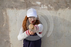 Young and beautiful red-haired woman with baseball cap, jacket with baseball bat defying camera. she is on grey concrete