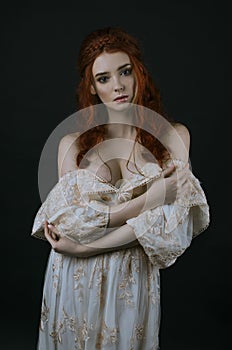 A young beautiful red-haired woman in a long vintage gold dress posing on a black background. A princess. Fairy tale. Fashion phot