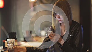 Young beautiful red-haired woman sitting in cafe or bar and using a smartphone