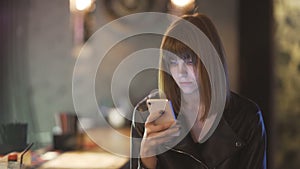 Young beautiful red-haired woman sitting in cafe or bar and using a smartphone