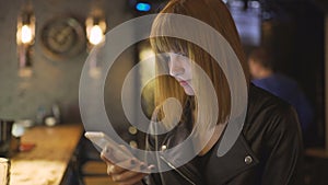 Young beautiful red-haired woman sitting in cafe or bar and using a smartphone