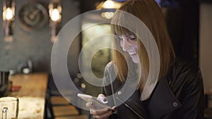 Young beautiful red-haired woman sitting in cafe or bar and using a smartphone