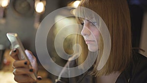 Young beautiful red-haired woman sitting in cafe or bar and using a smartphone