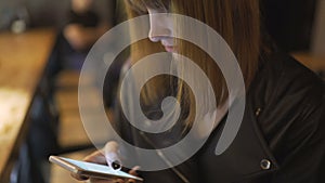 Young beautiful red-haired woman sitting in cafe or bar and using a smartphone