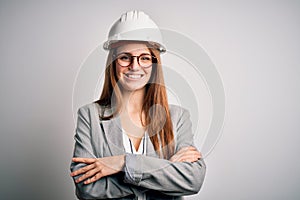 Young beautiful redhead architect woman wearing security helmet over white background happy face smiling with crossed arms looking