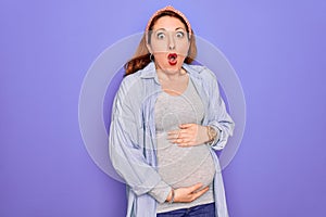 Young beautiful redhead pregnant woman expecting baby over isolated purple background afraid and shocked with surprise expression,