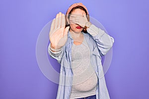 Young beautiful redhead pregnant woman expecting baby over isolated purple background covering eyes with hands and doing stop