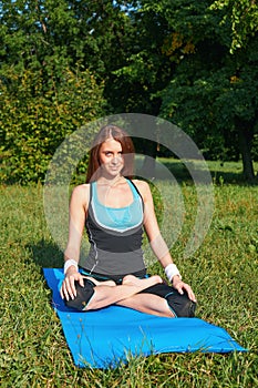 Young beautiful redhead woman doing yoga on a yoga mat. Performing yoga asanas in a green park. Sport, fitness and lifestyle