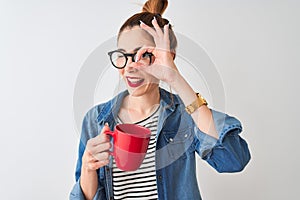 Young beautiful redhead woman drinking cup of coffee over isolated white background with happy face smiling doing ok sign with