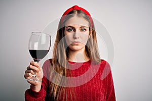 Young beautiful redhead woman drinking glass of red wine over isolated white background with a confident expression on smart face