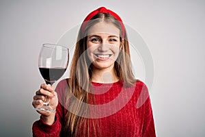 Young beautiful redhead woman drinking glass of red wine over isolated white background with a happy face standing and smiling