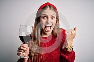 Young beautiful redhead woman drinking glass of red wine over isolated white background screaming proud and celebrating victory