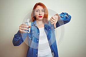 Young beautiful redhead woman drinking glass of water over white isolated background with angry face, negative sign showing