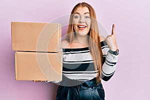 Young beautiful redhead woman holding delivery package smiling with an idea or question pointing finger with happy face, number