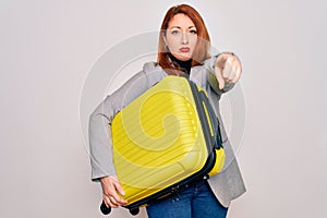 Young beautiful redhead woman holding suitcase prepared to business travel pointing with finger to the camera and to you, hand