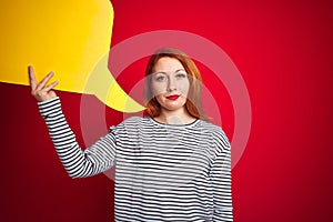 Young beautiful redhead woman holding yellow speech bubble over red isolated background with a confident expression on smart face