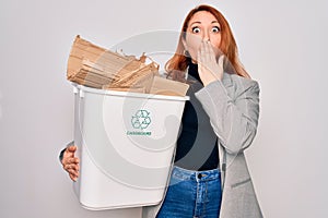 Young beautiful redhead woman recycling holding trash can with cardboard to recycle cover mouth with hand shocked with shame for