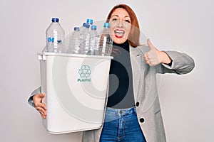 Young beautiful redhead woman recycling holding trash can with plastic bottles to recycle happy with big smile doing ok sign,