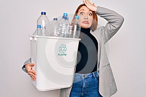 Young beautiful redhead woman recycling holding trash can with plastic bottles to recycle stressed with hand on head, shocked with