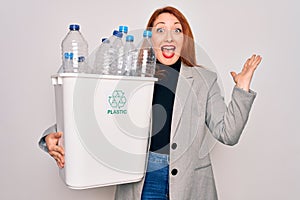 Young beautiful redhead woman recycling holding trash can with plastic bottles to recycle very happy and excited, winner