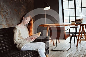 Young beautiful redhead woman relaxing at home in the autumn cozy evening and reading book