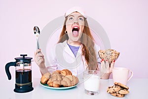 Young beautiful redhead woman sitting on the table having breakfast angry and mad screaming frustrated and furious, shouting with