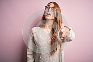 Young beautiful redhead woman wearing casual sweater and glasses over pink background pointing displeased and frustrated to the