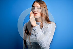 Young beautiful redhead woman wearing casual sweater over isolated blue background hand on mouth telling secret rumor, whispering