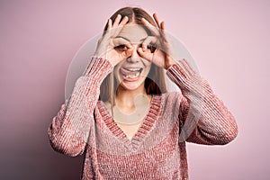 Young beautiful redhead woman wearing casual sweater over isolated pink background doing ok gesture like binoculars sticking