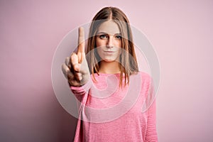 Young beautiful redhead woman wearing casual sweater over isolated pink background Pointing with finger up and angry expression,