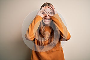 Young beautiful redhead woman wearing casual sweater over isolated white background doing ok gesture like binoculars sticking