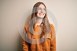 Young beautiful redhead woman wearing casual sweater over isolated white background looking away to side with smile on face,