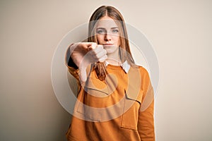 Young beautiful redhead woman wearing casual sweater over isolated white background looking unhappy and angry showing rejection