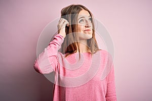 Young beautiful redhead woman wearing casual sweater over  pink background confuse and wondering about question