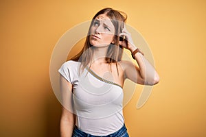 Young beautiful redhead woman wearing casual t-shirt over isolated yellow background confuse and wondering about question